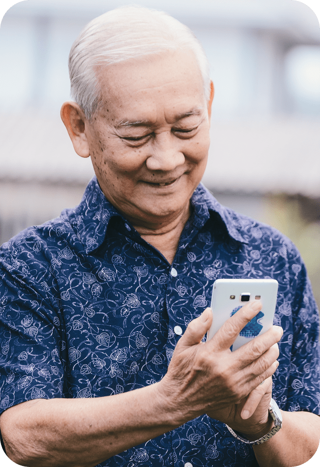 Elderly man with white hair smiling while using a smartphone outdoors in a blue patterned shirt